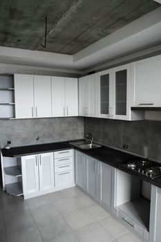 Modern minimalism style kitchen interior in monochrome tones. Custom kitchen with grey white facadesmdf and dark grey countertop with installed kitchen hood and sink. Modular kitchen from chipboard