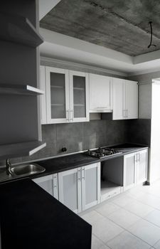 Modern minimalism style kitchen interior in monochrome tones. Custom kitchen with grey white facadesmdf and dark grey countertop with installed kitchen hood and sink. Modular kitchen from chipboard