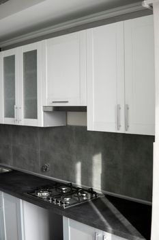 Modern minimalism style kitchen interior in monochrome tones. Custom kitchen with grey white facadesmdf and dark grey countertop with installed kitchen hood and sink. Modular kitchen from chipboard