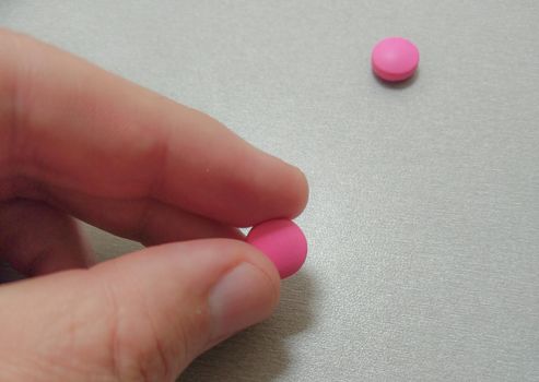 Hand picking up a pink pill painkiller