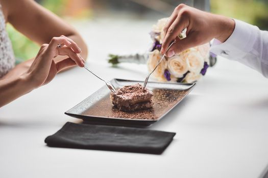 A man and a young girl eat a cake. A date in a cafe. A bouquet of flowers in the background in defocus. Hands close-up. Without a face. Meeting of lovers in a restaurant.