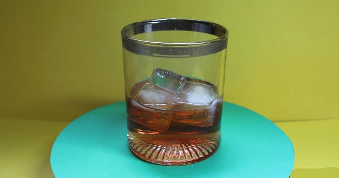 Glass with refreshing whiskey and ice cubes is rotating