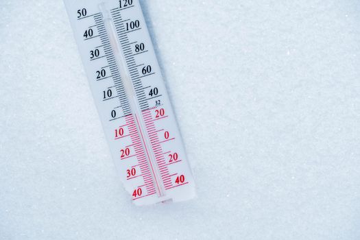 The thermometer lies on the snow and shows a negative temperature in cold weather on the blue sky.Meteorological conditions with low air and ambient temperatures.Climate change and global warming