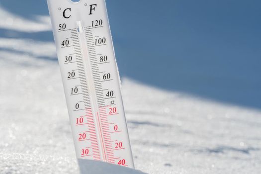 The thermometer lies on the snow and shows a negative temperature in cold weather on the blue sky.Meteorological conditions with low air and ambient temperatures.Climate change and global warming