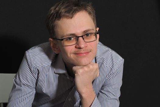 Portrait of a young man of European appearance in glasses and a light shirt, smiling. High quality photo