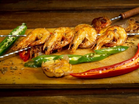 Japanese seafood. Fried spicy shrimps with herbs on wooden skewers served on black slate, close up view.