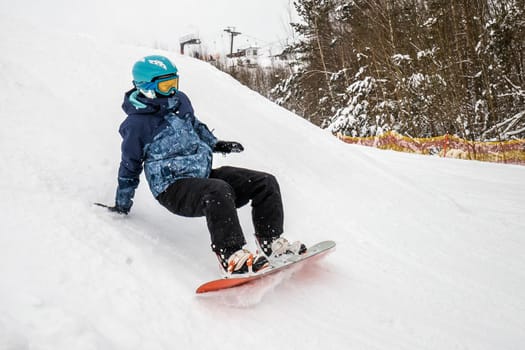 Person go down on a snowboard from the mountainside along a specially prepared track. They make mistakes and fall. Ski vacation. January, Logoisk, Belarus