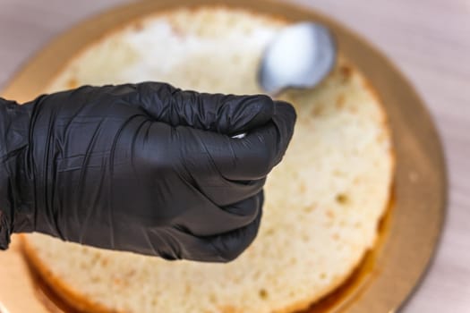 Female hand in black glove pours milk on a cheesecake with coconut, on wooden table.