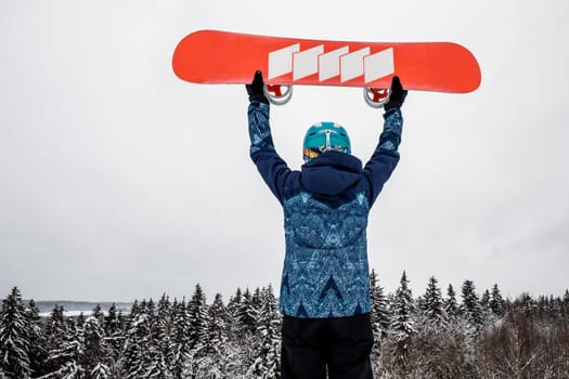 Female in a blue suit standing with a snowboard on a large snow slope. Snowboarder holds the snowboard over his head. Skiing holidays. Logoisk, Belarus