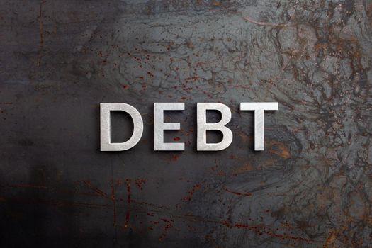 the word debt laid with silver letters on raw rusted steel sheet surface in flat lay perspective.