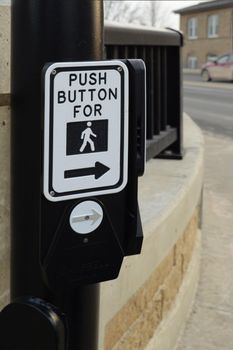 A closeup view of a new modern crosswalk push button at a busy street intersection.