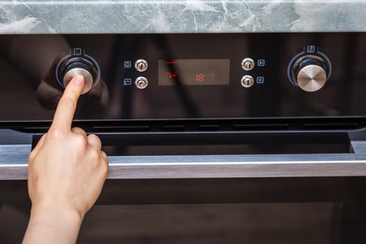 Female hand turning on the oven to make a cake at home. Close-up of the oven knob. View of the black electric oven, knob with a hot air icon. The concept of heating food, baking a cake.