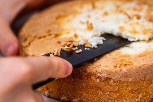 Female hand cuts sponge cheesecake with coconut, on wooden table.