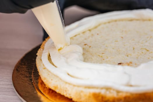 Female hand in black glove squeezes out cream on a cheesecake with coconut.