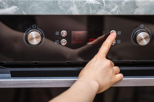 Female hand turning on the oven to make a cake at home. Close-up of the oven knob. View of the black electric oven, knob with a hot air icon. The concept of heating food, baking a cake.