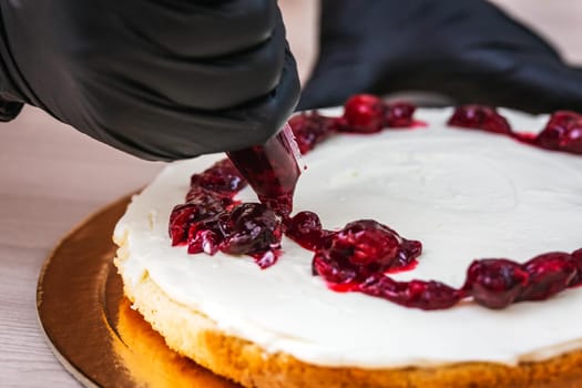 Female hand in black glove squeezes out cherry confiture on a cheesecake with coconut.