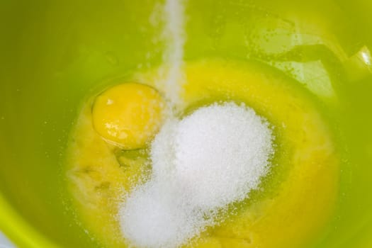 Adding sugar to the eggs and making homemade cake.