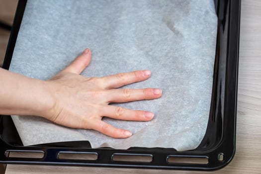 Hand holds baking paper on a tray. Preparing homemade cake.