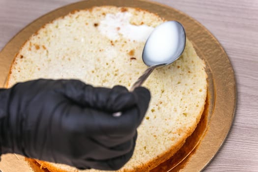 Female hand in black glove pours milk on a cheesecake with coconut, on wooden table.