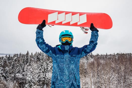 Female in a blue suit standing with a snowboard on a large snow slope. Snowboarder holds the snowboard over his head. Skiing holidays. Logoisk, Belarus