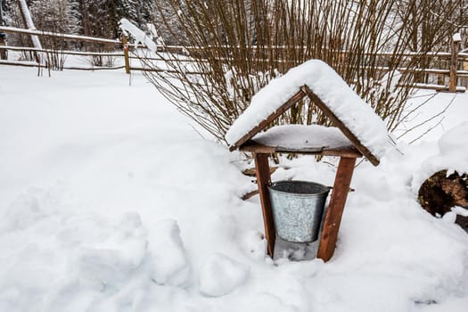 Decorated wooden house with textured wall and bucket covered with a heavy snow in the village in Belarus.
