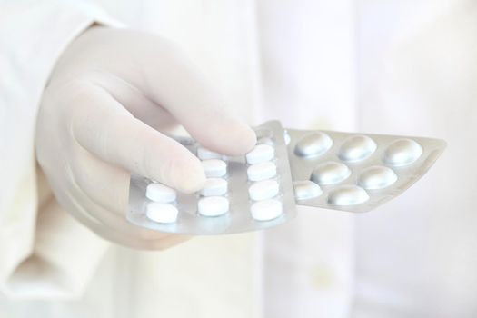Male hand in white surgical glove holding pill blisters