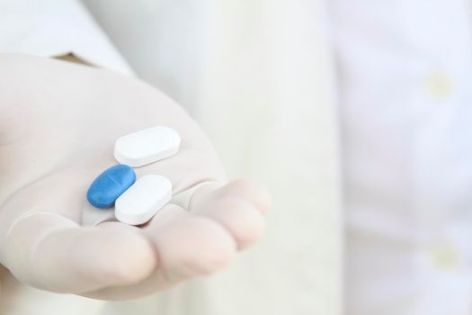 Male hand in white surgical glove holding pills