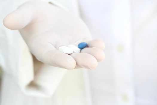 Male hand in white surgical glove holding pills