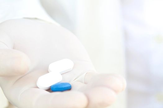 Male hand in white surgical glove holding pills