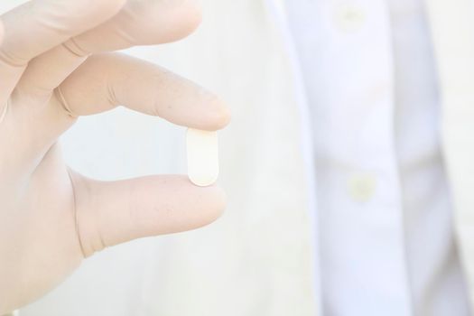 Male hand in white surgical glove holding a pill