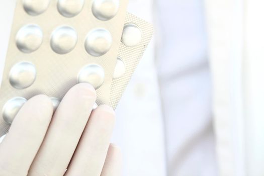 Male hand in white surgical glove holding pill blisters