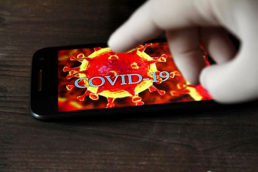 Madrid, Spain- April 23, 2020: Hand in surgical glove pointing at a mobile phone with picture of covid-19 word written on it