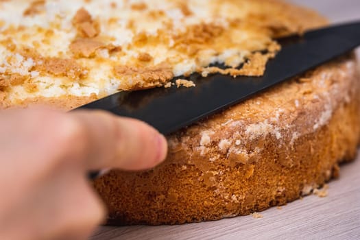 Female hand cuts sponge cheesecake with coconut, on wooden table.