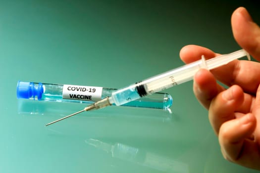 Hand holding Syringe next to test tube with vaccine for Covid-19 virus