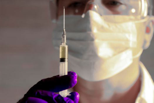 Laboratory assistant wearing protective glasses and surgery gloves holding a syringe with Covid-19 virus vaccine
