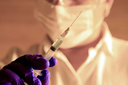 Laboratory assistant wearing protective glasses and surgery gloves holding a syringe with Covid-19 virus vaccine