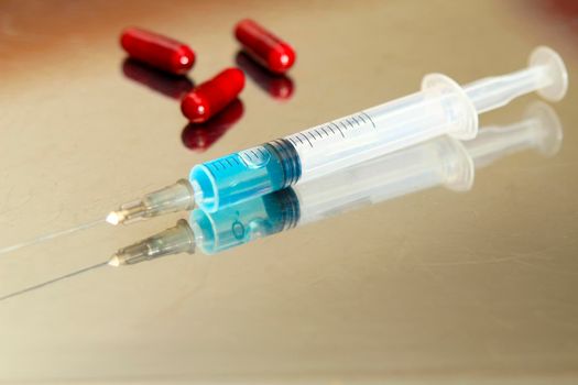 Syringe next to red capsules on metallic surface