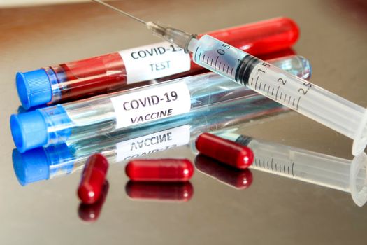 Syringe next to capsules and test tubes with blood and vaccine for Covid-19 virus