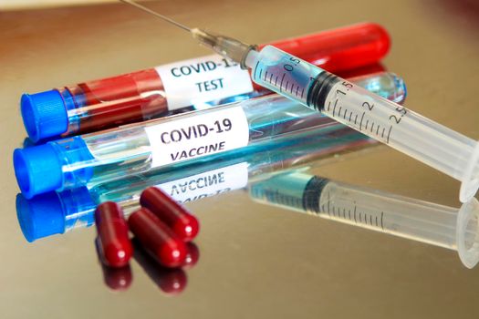 Syringe next to capsules and test tubes with blood and vaccine for Covid-19 virus