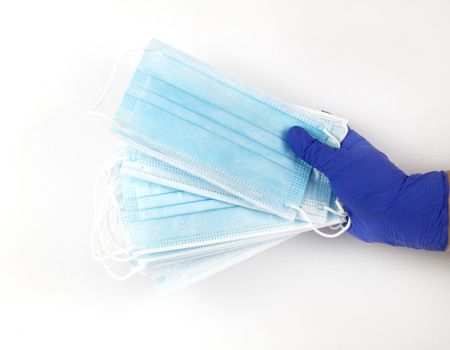 Hand on blue surgical gloves hanging Disposable Medical masks on white background. Covid-19 and healthcare concept