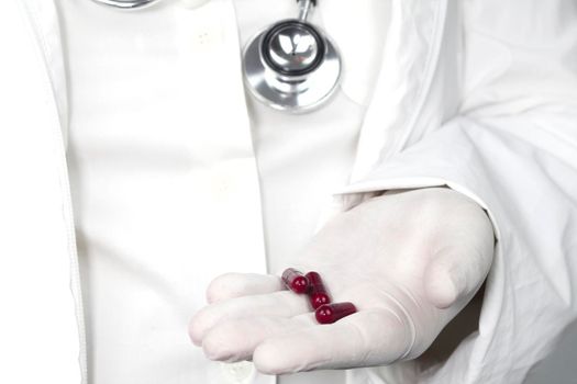Doctor in white surgical gloves and wearing stethoscope holding red capsules