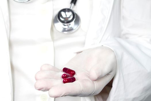 Doctor in white surgical gloves and wearing stethoscope holding red capsules