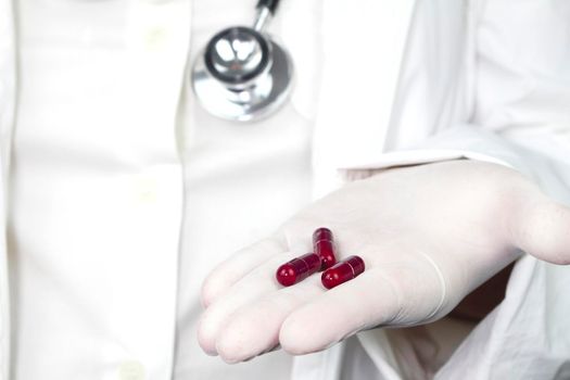 Doctor in white surgical gloves and wearing stethoscope holding red capsules