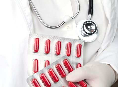 Doctor in white surgical gloves and wearing stethoscope holding red capsule blisters