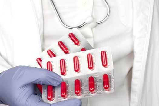 Doctor in blue surgical gloves and wearing stethoscope holding red capsule blisters