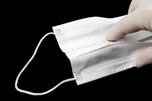 Hand on surgical gloves hanging Disposable Medical mask on black background. Covid-19 and healthcare concept