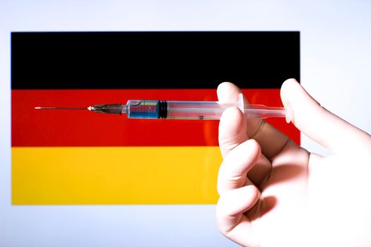 Hand in surgery glove holding syringe with covid vaccine. Germany flag in the background