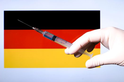 Hand in surgery glove holding syringe with covid vaccine. Germany flag in the background