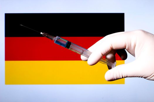 Hand in surgery glove holding syringe with covid vaccine. Germany flag in the background