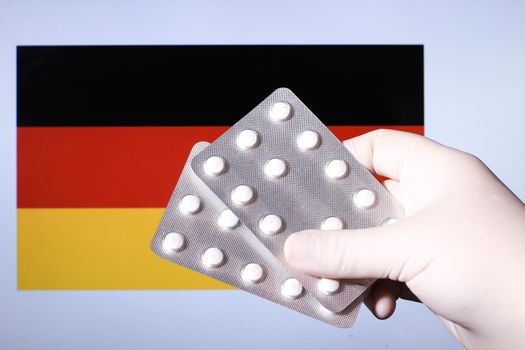 Hand in surgical glove holding pill blisters. German flag in the background